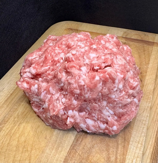 A mound of raw ground meat with visible fat marbling sits on a wooden cutting board against a dark background.